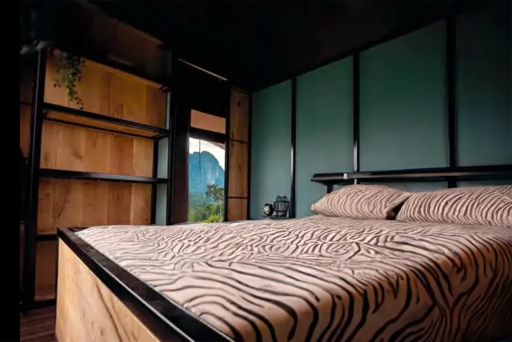 Chambre de lodge de luxe avec un lit grand format et une couverture à motif zèbre, offrant une vue sur les montagnes verdoyantes.